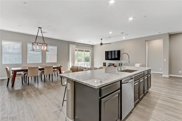 kitchen featuring baseboards, dishwasher, a kitchen island with sink, light wood-style floors, and a sink