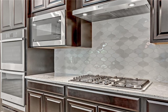 kitchen with stainless steel appliances, backsplash, dark brown cabinetry, and under cabinet range hood