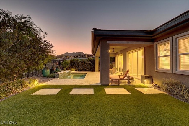 yard at dusk featuring a ceiling fan, a patio area, and a fenced backyard