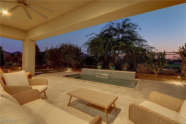 patio terrace at dusk with a fenced backyard, outdoor lounge area, a ceiling fan, and an in ground hot tub