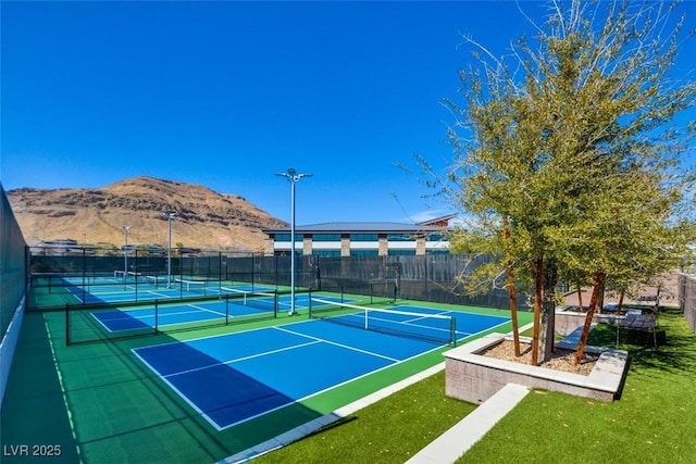 view of tennis court with fence, a mountain view, and a yard