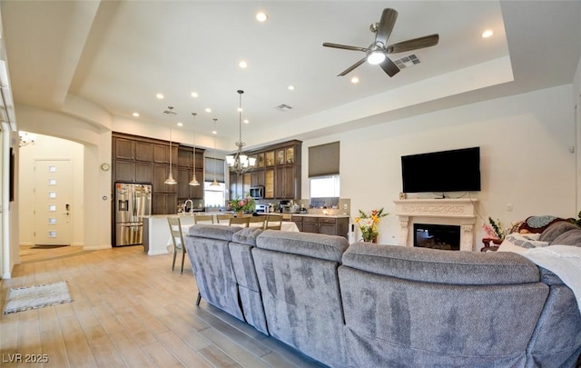 living area with visible vents, a glass covered fireplace, a tray ceiling, light wood-style floors, and recessed lighting