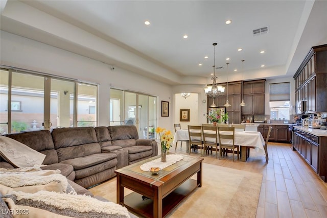 living room with recessed lighting, a notable chandelier, visible vents, light wood-style floors, and a raised ceiling