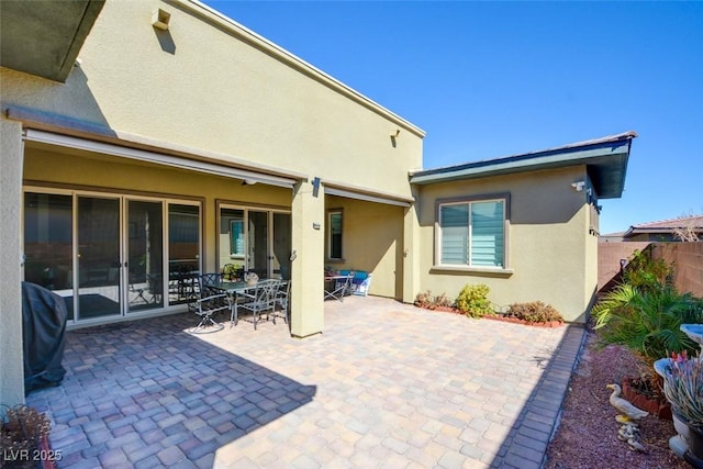 back of house with outdoor dining area, a patio area, fence, and stucco siding