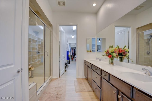 full bath with a spacious closet, a sink, a shower stall, and double vanity