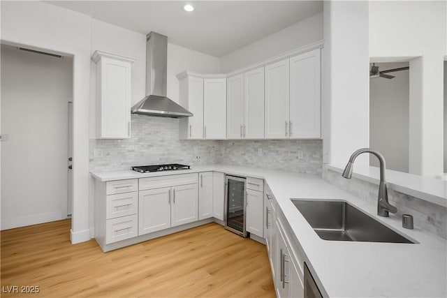 kitchen featuring black gas cooktop, wine cooler, a sink, white cabinetry, and wall chimney exhaust hood