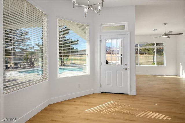 doorway to outside with ceiling fan with notable chandelier, light wood-type flooring, and baseboards