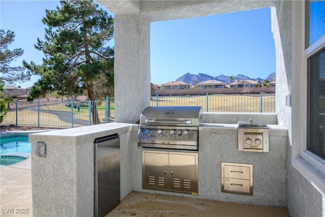 view of patio / terrace with a pool with connected hot tub, area for grilling, fence, and an outdoor kitchen