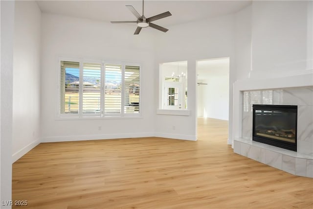 unfurnished living room with light wood finished floors, a fireplace, baseboards, and a ceiling fan