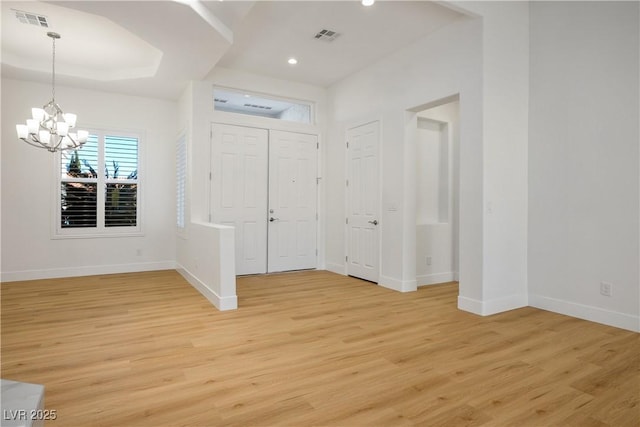 foyer with a tray ceiling, visible vents, and light wood finished floors