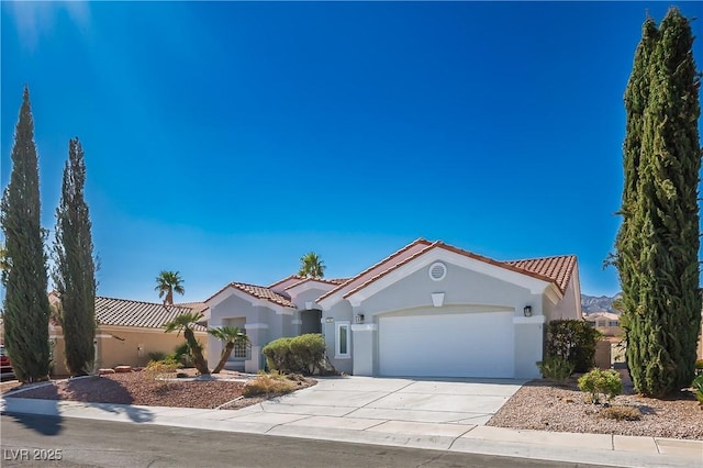 mediterranean / spanish-style home featuring an attached garage, driveway, a tile roof, and stucco siding