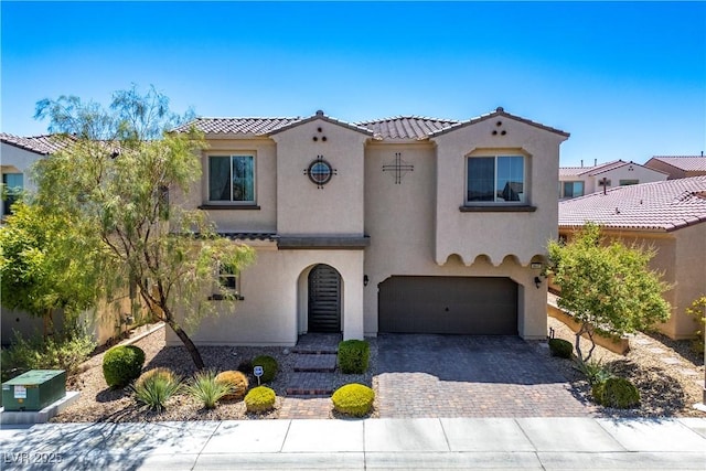 mediterranean / spanish-style house with a garage, decorative driveway, a tile roof, and stucco siding