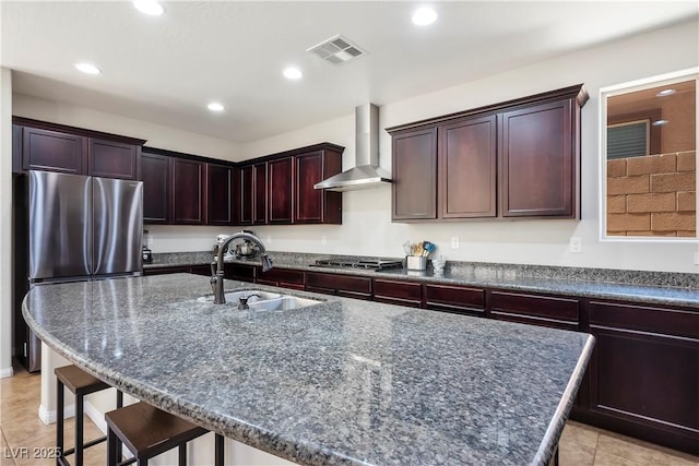 kitchen with stainless steel appliances, visible vents, a sink, wall chimney range hood, and a kitchen bar