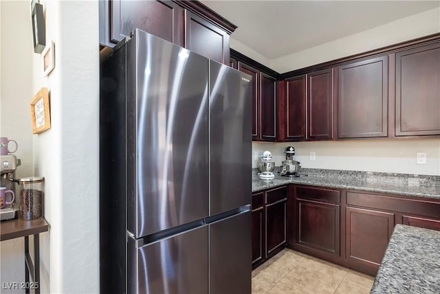 kitchen with light tile patterned floors, stone countertops, and freestanding refrigerator