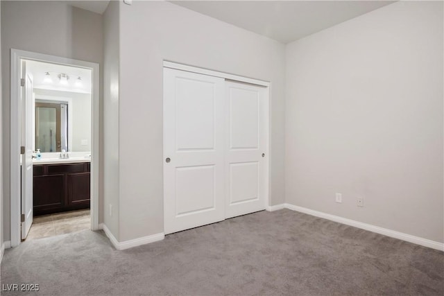 unfurnished bedroom with a closet, baseboards, light colored carpet, ensuite bath, and a sink