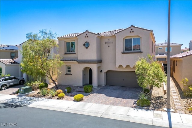 mediterranean / spanish-style home featuring a tiled roof, decorative driveway, an attached garage, and stucco siding