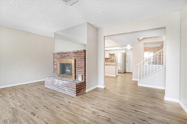 unfurnished living room featuring visible vents, baseboards, wood finished floors, stairs, and a brick fireplace