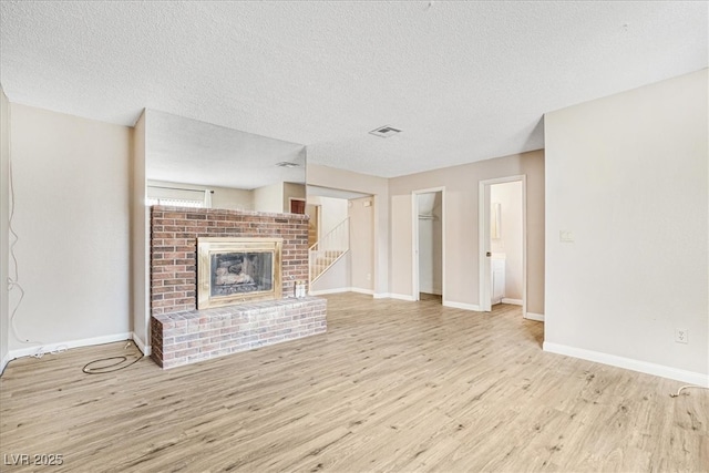 unfurnished living room featuring a brick fireplace, wood finished floors, visible vents, and baseboards