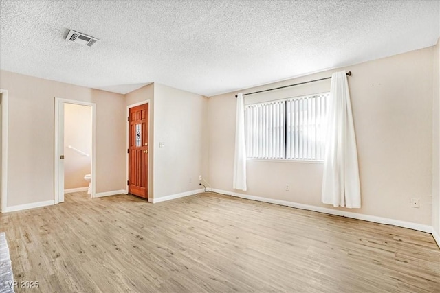 spare room featuring a textured ceiling, wood finished floors, visible vents, and baseboards