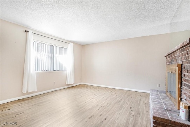 unfurnished living room with a textured ceiling, a fireplace, baseboards, and wood finished floors