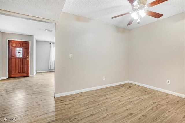 empty room with light wood-type flooring, ceiling fan, a textured ceiling, and baseboards