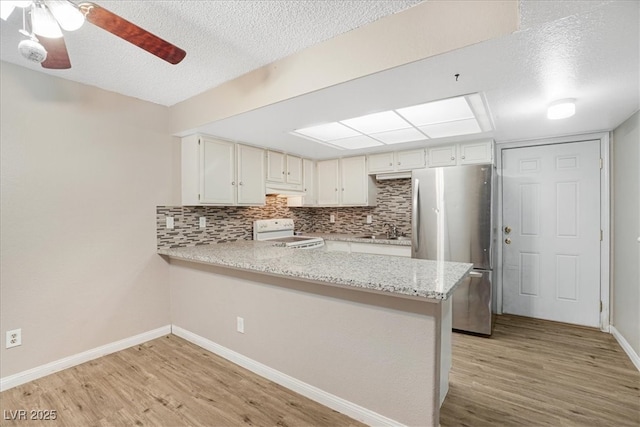 kitchen featuring a peninsula, electric range, a sink, freestanding refrigerator, and light wood finished floors