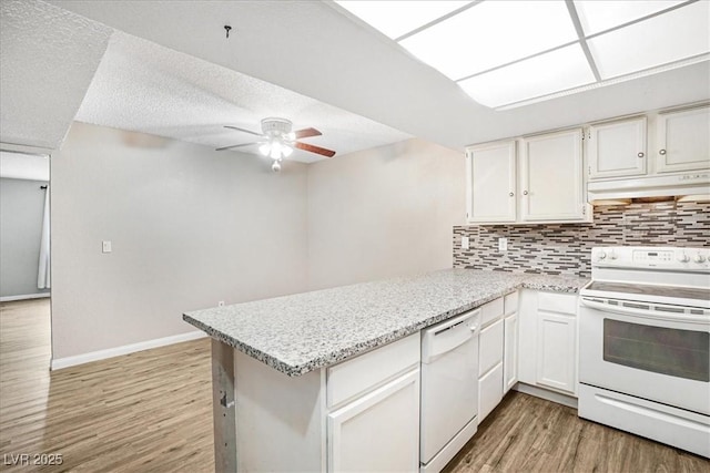 kitchen with under cabinet range hood, a peninsula, white appliances, white cabinets, and backsplash