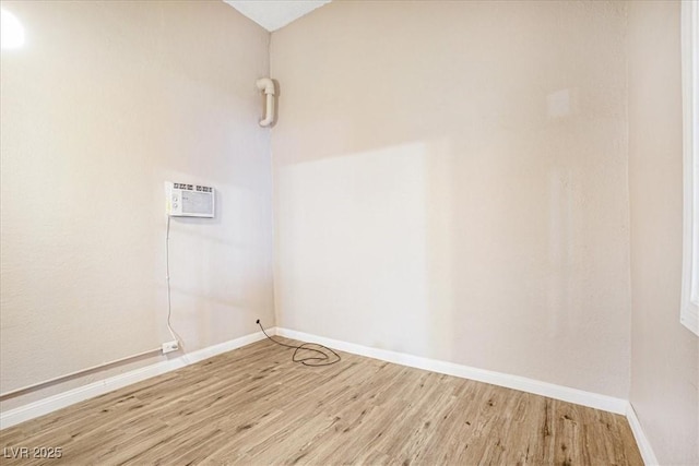 unfurnished room featuring baseboards, wood finished floors, and a wall mounted air conditioner