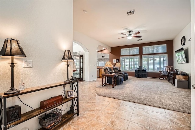 living area featuring visible vents, light tile patterned flooring, arched walkways, ceiling fan, and light carpet