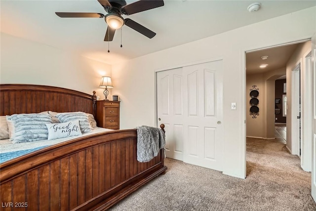 bedroom with a closet, light colored carpet, arched walkways, and ceiling fan