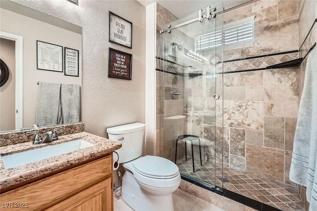 bathroom featuring vanity, toilet, a textured wall, and a stall shower