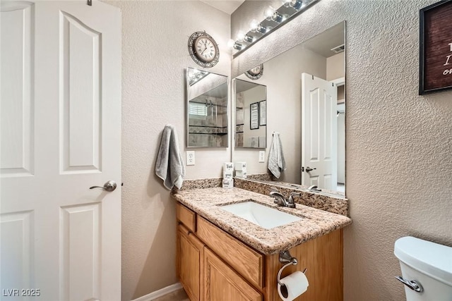 bathroom with visible vents, toilet, vanity, and a textured wall