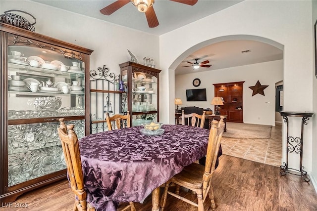 dining space featuring arched walkways, visible vents, ceiling fan, and wood finished floors