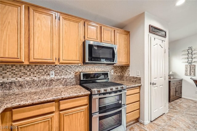 kitchen featuring baseboards, light stone countertops, tasteful backsplash, and appliances with stainless steel finishes