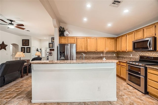 kitchen with visible vents, a center island with sink, decorative backsplash, appliances with stainless steel finishes, and arched walkways