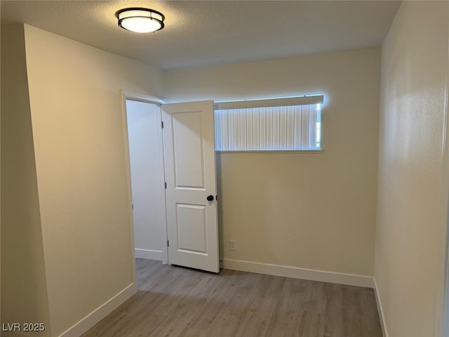 unfurnished room with light wood-type flooring, a textured ceiling, and baseboards