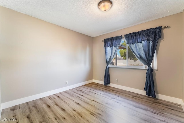 empty room with a textured ceiling, baseboards, and wood finished floors