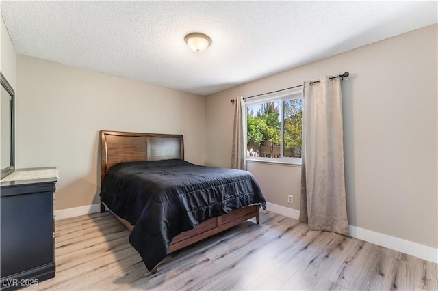 bedroom with light wood finished floors, baseboards, and a textured ceiling