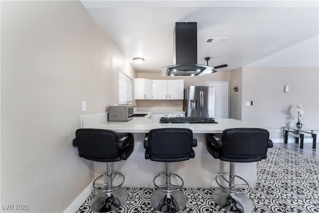 kitchen featuring stainless steel fridge, visible vents, island exhaust hood, light countertops, and a sink