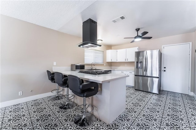 kitchen with island exhaust hood, visible vents, light countertops, appliances with stainless steel finishes, and a peninsula