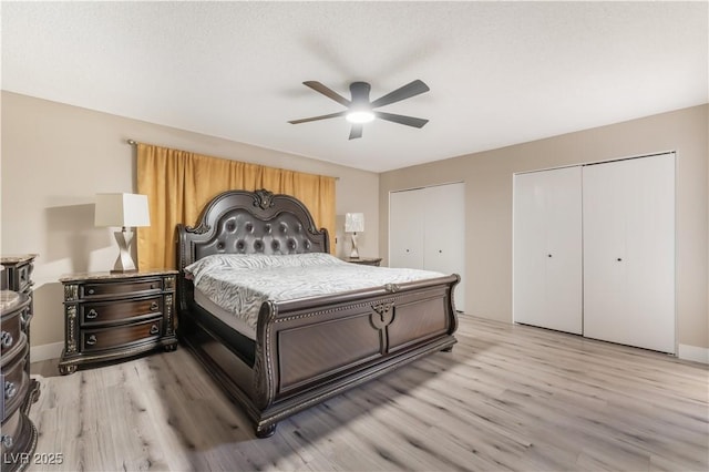 bedroom with light wood finished floors, two closets, and a ceiling fan