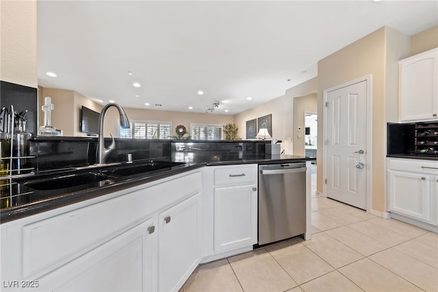 kitchen featuring stainless steel dishwasher, dark countertops, a sink, and white cabinets