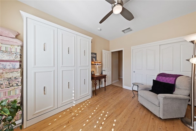 living area featuring a ceiling fan, baseboards, visible vents, and light wood finished floors