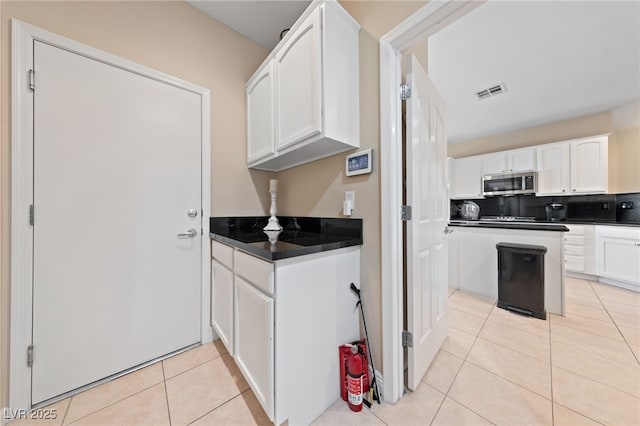 kitchen featuring light tile patterned floors, stainless steel microwave, visible vents, and white cabinets