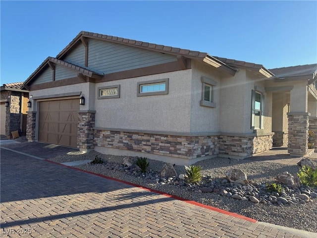 view of property exterior featuring a garage, stone siding, decorative driveway, and stucco siding