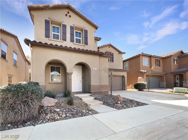 mediterranean / spanish home featuring a garage, driveway, central air condition unit, and stucco siding