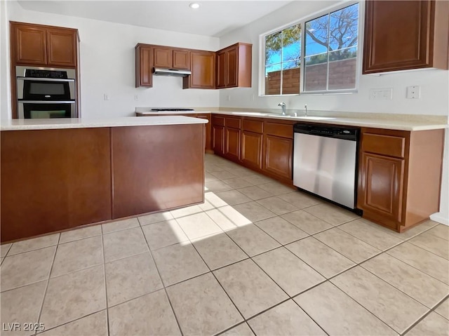 kitchen featuring light tile patterned floors, brown cabinetry, stainless steel appliances, light countertops, and under cabinet range hood