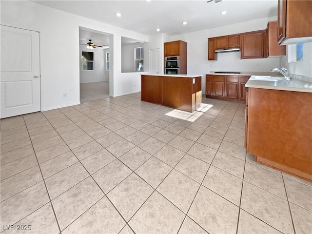 kitchen with brown cabinets, light tile patterned floors, double oven, a kitchen island, and stovetop