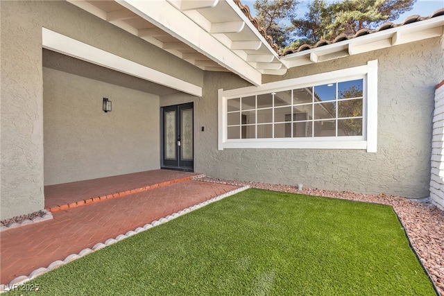 doorway to property featuring french doors, a lawn, and stucco siding