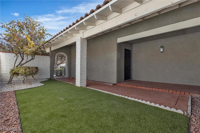 entrance to property featuring a tile roof, fence, a lawn, and stucco siding